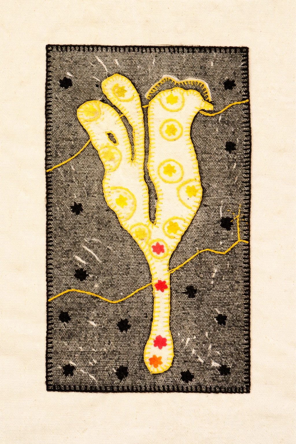A stitched yellow flower with red details on a dark textured ground
